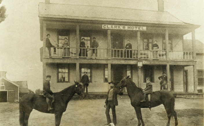 Exterior of Clark's Hotel in Chazy. There is a man standing in front of the building with two horses.